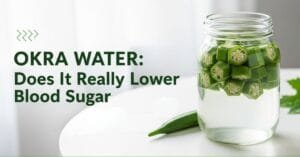 Glass of okra water with sliced okra pods soaking inside, placed on a clean white surface. The image highlights the green okra pieces and the gel-like texture released into the water, representing a natural home remedy often used to support healthy blood sugar levels